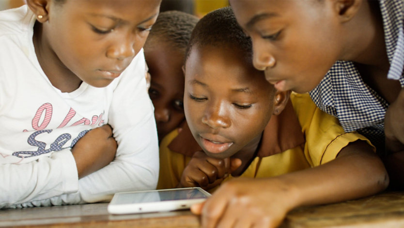 Four children gathered around a tablet, focused on the screen.