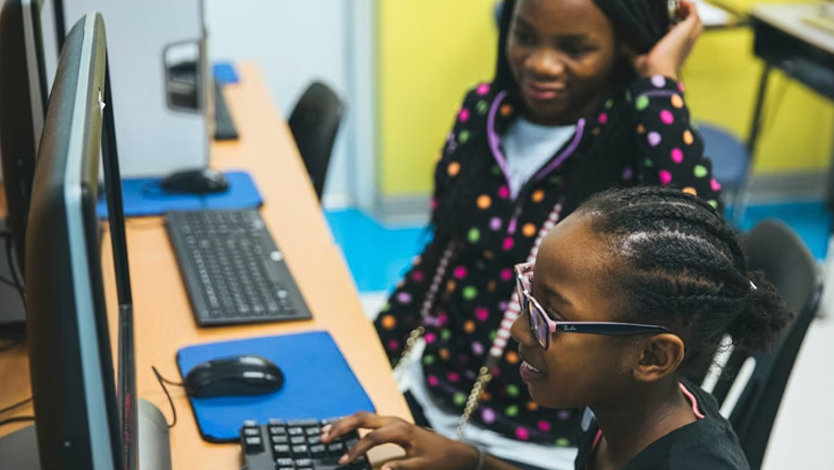 Two children in a computer lab use a computer.