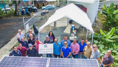 A group of people pose behind a solar panel.