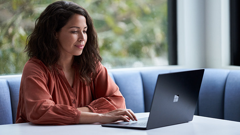 A businesswoman working on a laptop at a table by a window.