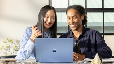 Two business people working on a laptop at a table by a window.