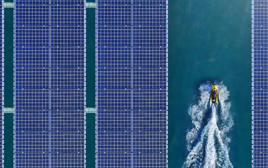 Aerial view of a floating solar array with a jet ski passing between the panels.