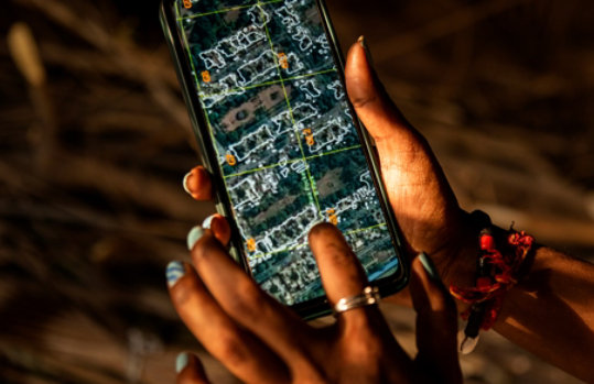 Close-up of a hand holding a phone displaying a map of satellite imagery.