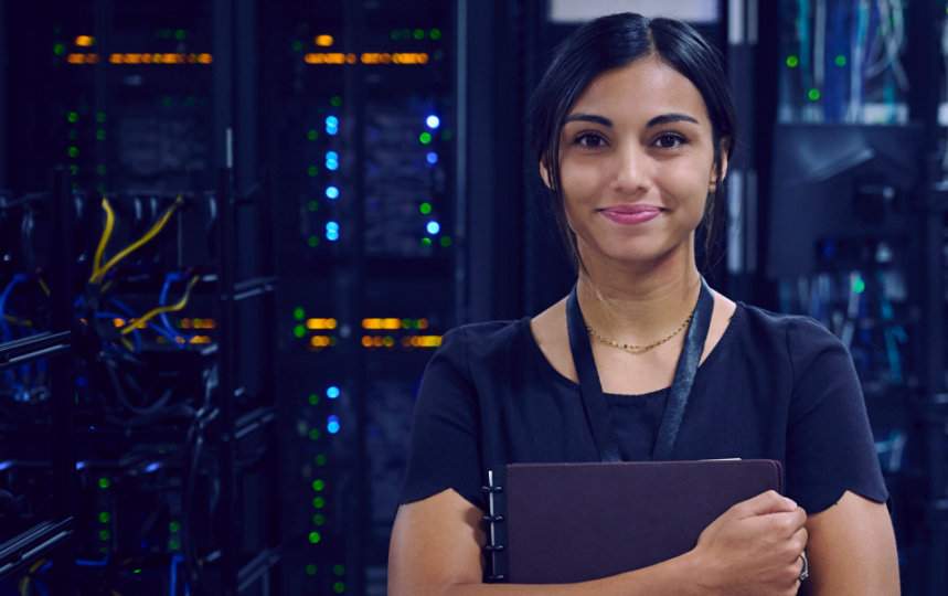 Female IT worker standing in a server room holding a folder and smiling.