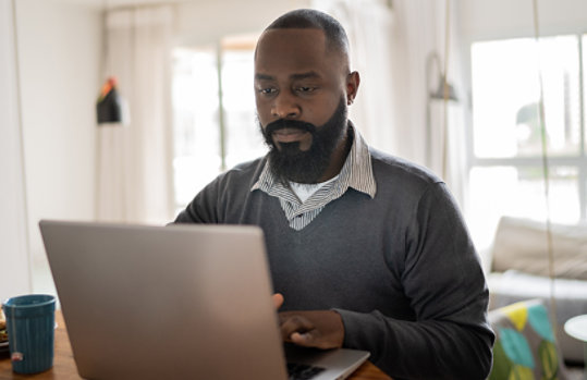A man wearing business casual attire working on a laptop in a home environment.