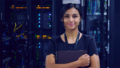 Female IT worker standing in a server room holding a folder and smiling.
