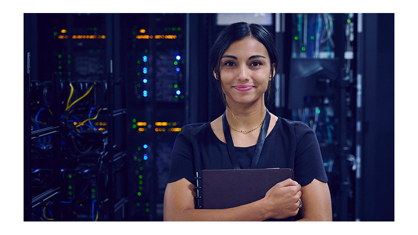 Female IT worker standing in a server room holding a folder and smiling.