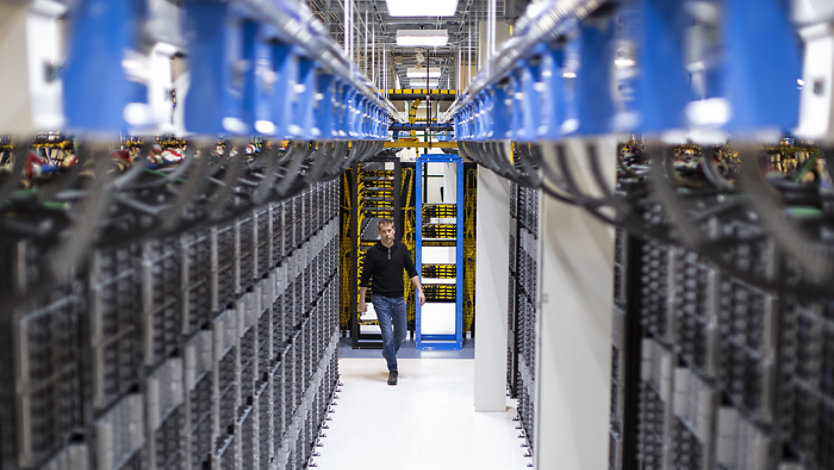 Technician walking down a narrow aisle between rows of server racks in a data center.
