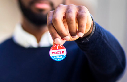 A man in the backdrop is holding an I-Voted-Today sticker.