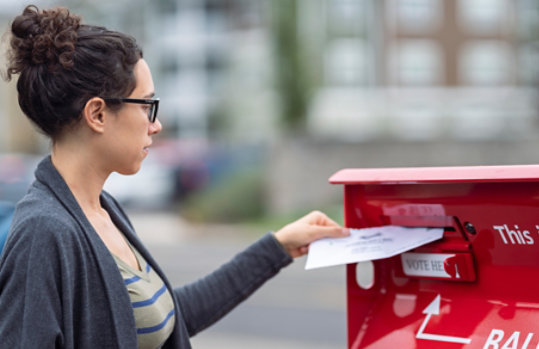 Young adult woman placing her ballot in an official ballot box.