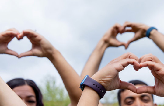 People holding their arms above their hands and each positioning their hands in the shape of a heart.