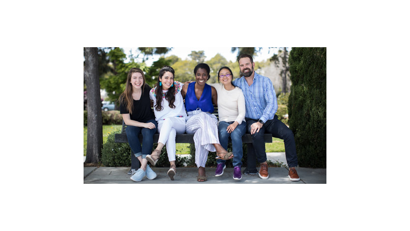 A small group of diverse people sit together on a bench.