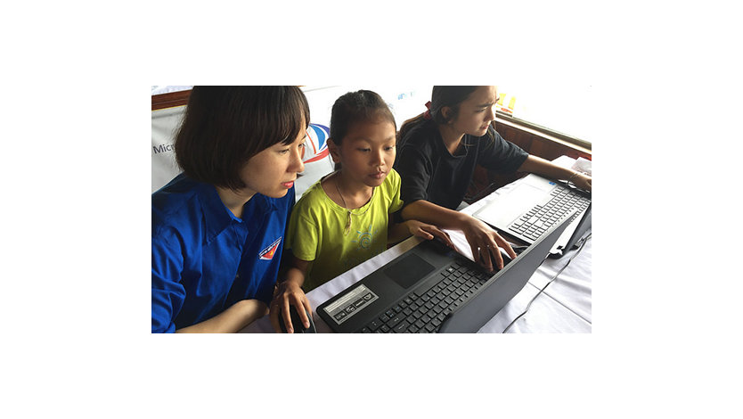 Two young girls work on laptops while their teacher watches.