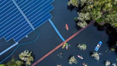 Aerial view of floating solar cells for clean energy alongside people in small colorful kayaks and a blue flat bottom boat.