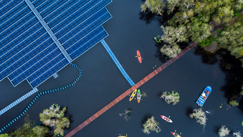 Aerial view of floating solar cells for clean energy alongside people in small colorful kayaks and a blue flat bottom boat.