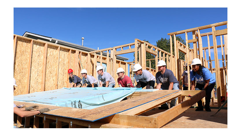 A team of workers wearing hard hats lifting the wall of a house under construction.