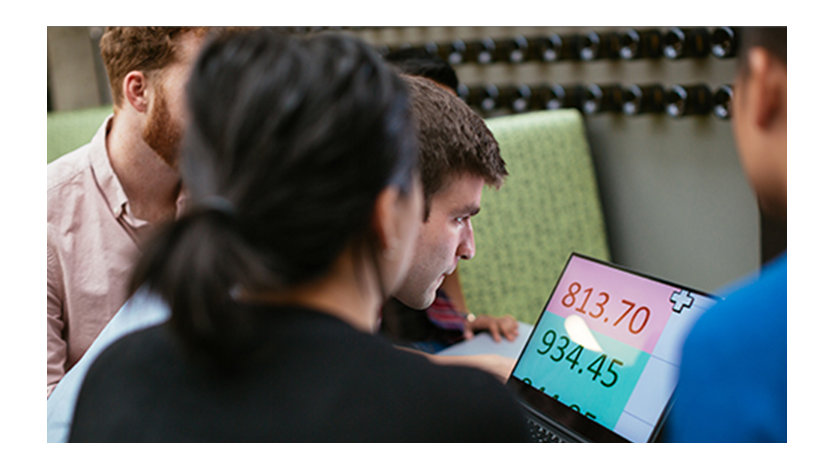 Four young adults look at an enlarged Excel spreadsheet on a laptop.