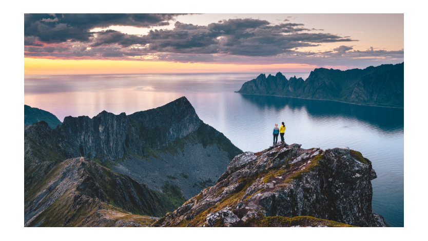 Sweeping landscape of two friends admiring the sunset from top of a high cliff in Northern Norway.