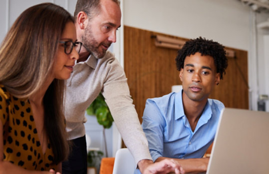 Three coworkers collaborating around a laptop computer.