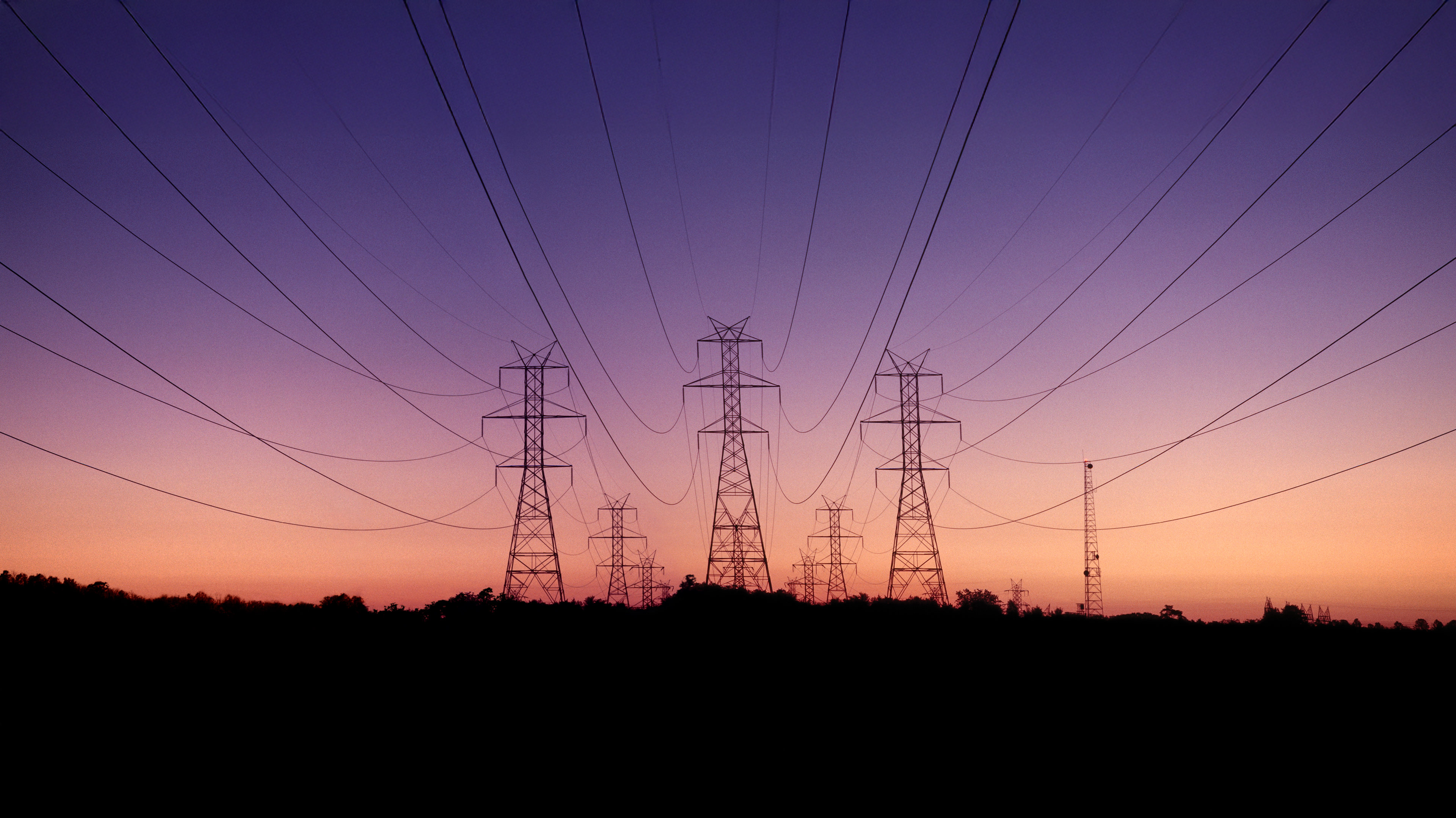High-voltage power lines and towers silhouetted against a colorful sunset sky.