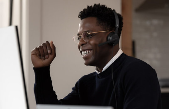 A man wearing a headset smiles in an office setting.