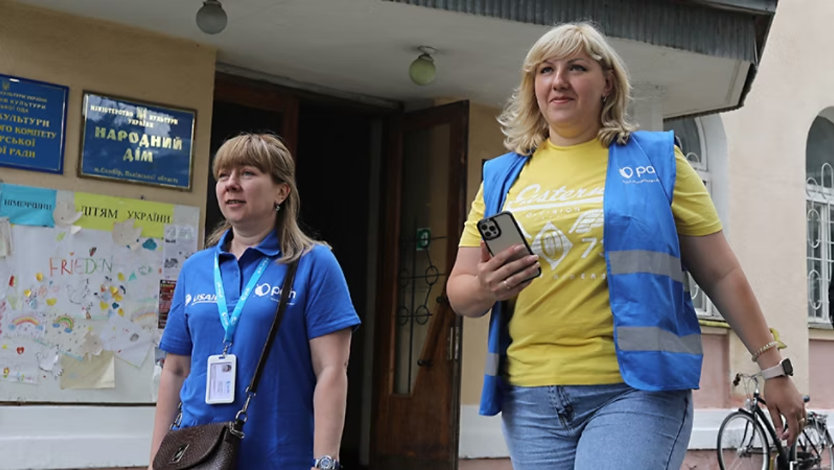 Two Humanitarian Action workers wearing vests and lanyards coordinate aid to displaced Ukranians.