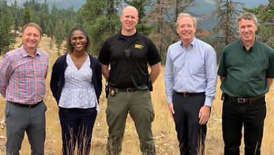 Group of people including a sheriff and Microsoft Vice Chair and President, Brad Smith, standing in a grass field with trees in the background.