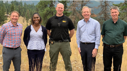 Group of people including a sheriff and Microsoft Vice Chair and President, Brad Smith, standing in a grass field with trees in the background.