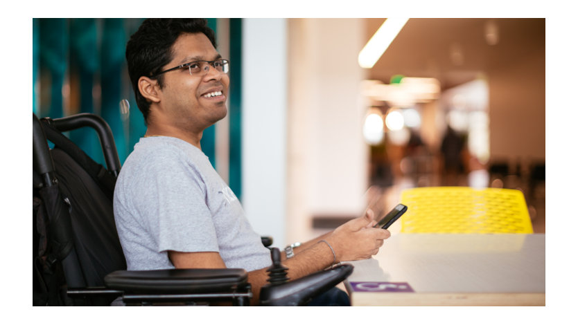 Man using a mobile phone sitting at a wheelchair-accessible table