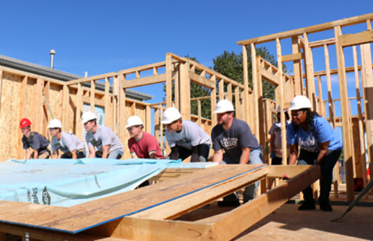 A group of volunteers lifting a house frame together
