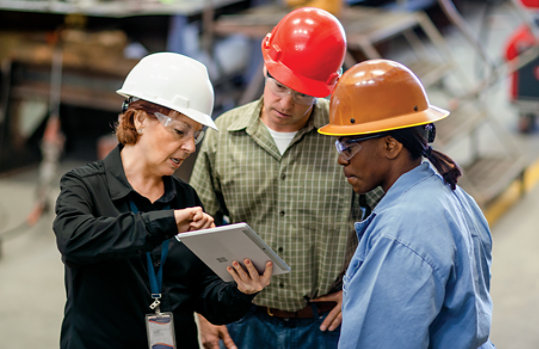 Three manufacturing workers look at a tablet device in a factory setting.