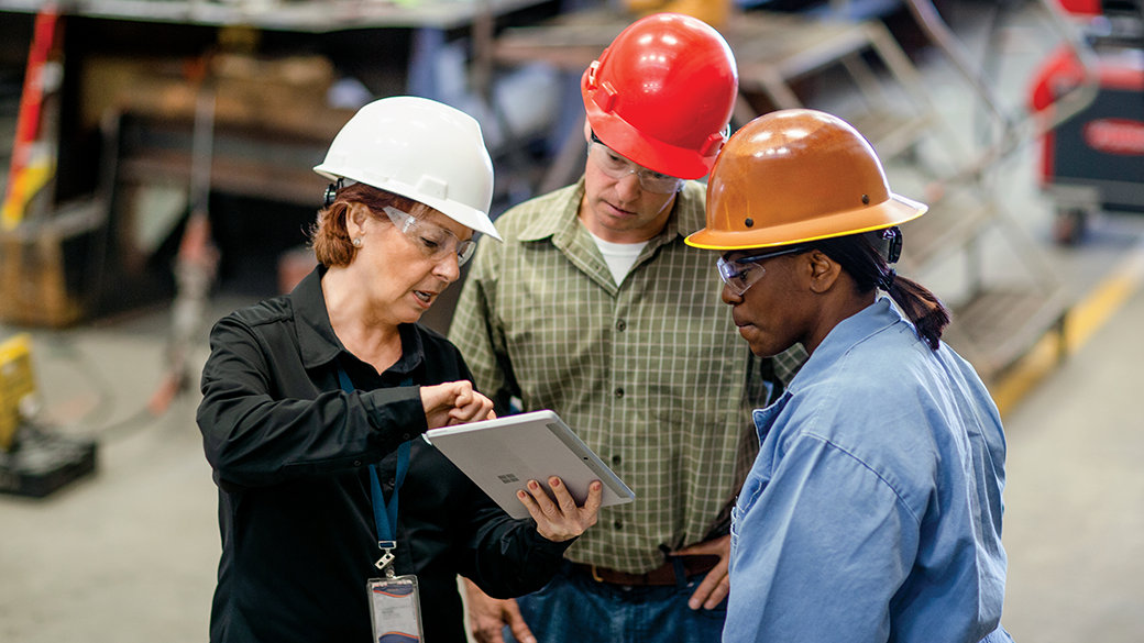 Three manufacturing workers look at a tablet device in a factory setting.