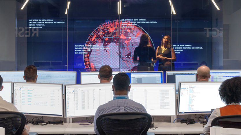 Operations center with analysts at multiple monitors and a large world-data display.