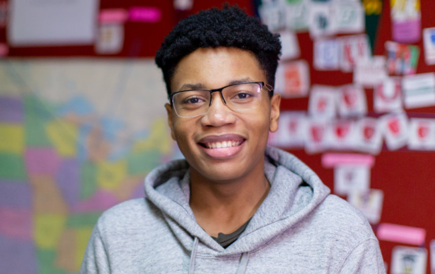 A smiling high school student standing in a classroom.