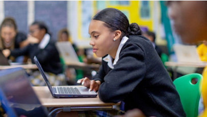 Young people in uniforms work on laptops in a classroom.