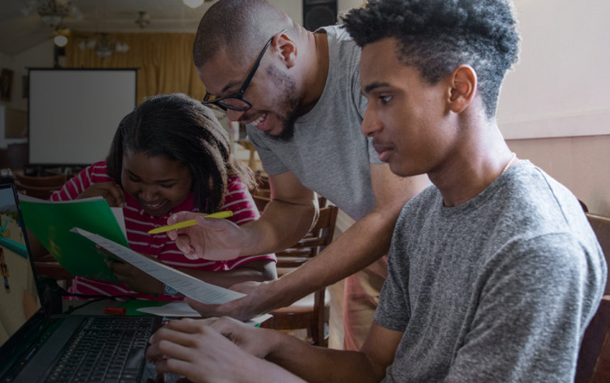 An adult helps two young people playing Minecraft.