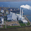 Coastal power plant with tall chimneys and nearby wind turbines.