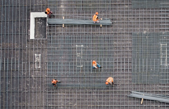 Aerial view of workers installing a steel rebar grid on a construction site.