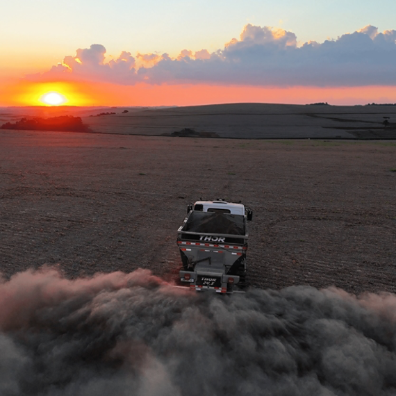 A tractor spreads basalt across a field at sunrise.