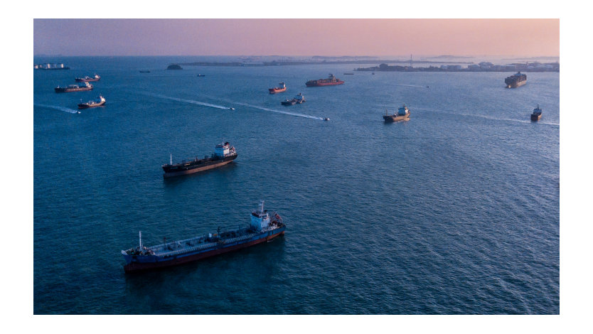 Aerial view of cargo ships waiting offshore to dock in a harbor.