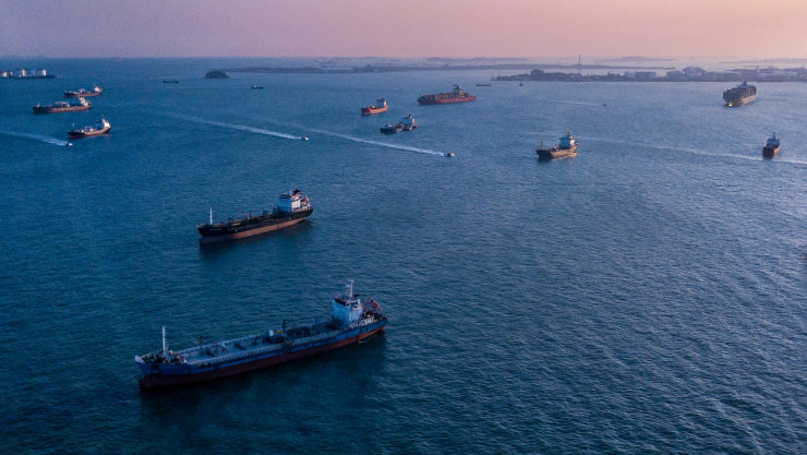 Aerial view of cargo ships waiting offshore to dock in a harbor.