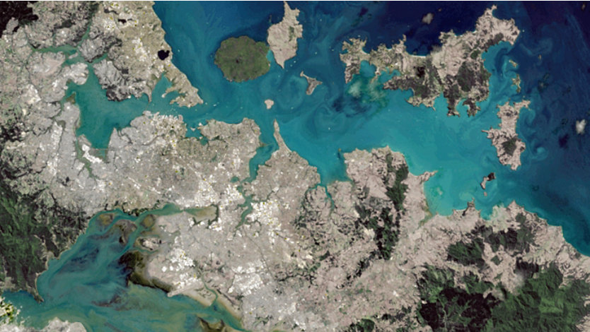 Satellite view of a coastal region showing bays, peninsulas, urban areas, and green forested land.