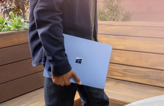 Adult male outside holding Surface Laptop (7th edition) Copilot+ PC in Sapphire