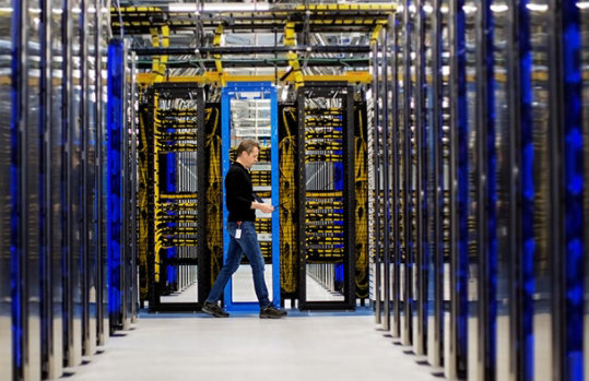 Engineer walking between server racks in a datacenter, holding a tablet.