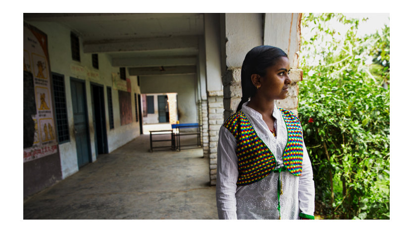 Profile view of a young woman standing in the outdoor corridor of a school.