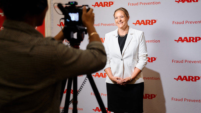 Woman posing for a camera in front of an AARP event backdrop.