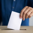 Hand inserting a ballot into a ballot box slot.