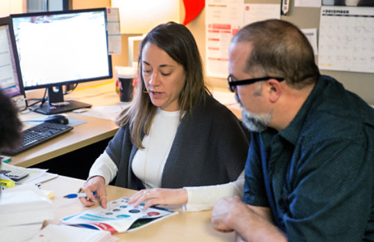 Two people reviewing paperwork together at a desk in an office environment.