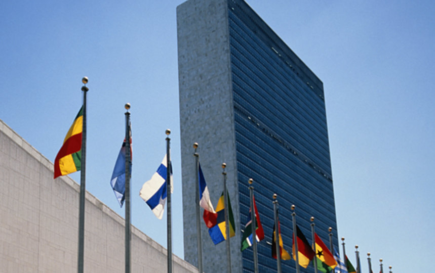 United Nations Headquarters with a row of international flags in front of the building under a clear blue sky.