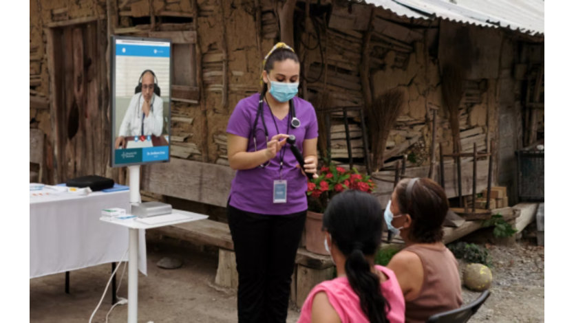 A nurse speaks with patients in a rural area with a telehealth screen in the background.